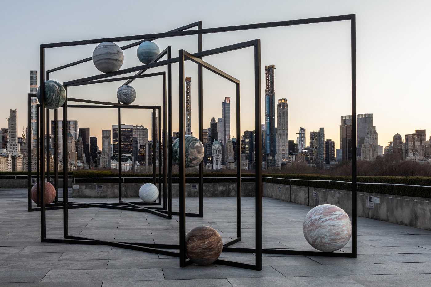 不同颜色的大石球，悬挂在黑色钢框中，映衬着曼哈顿的天际线