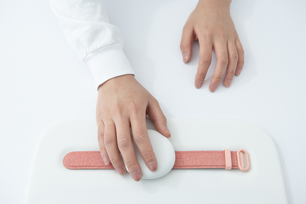 照片上的手拿着一个白色的球状物体在粉红色的腕带。