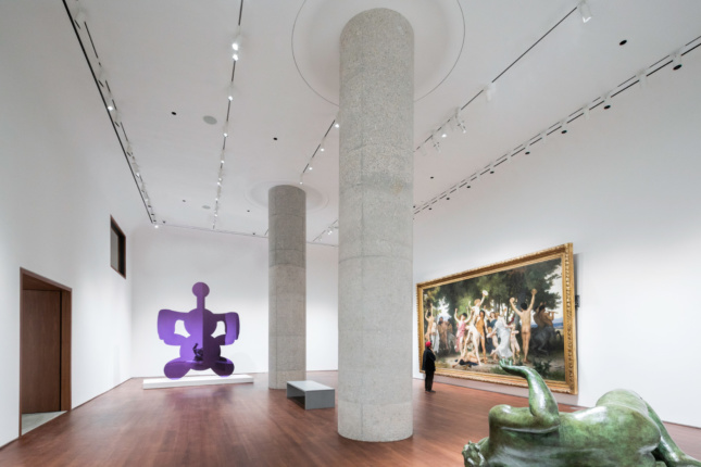 白色画廊的照片，中央有胡桃木地板和两根混凝土柱子