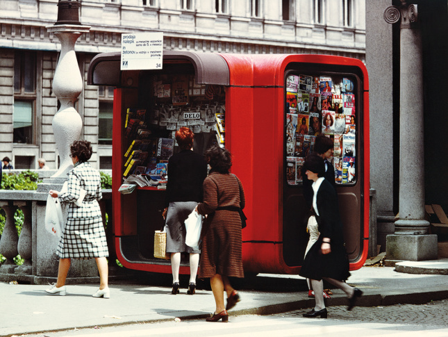 一个圆形的红色报亭在街上卖杂志的照片，人们从旁边走过
