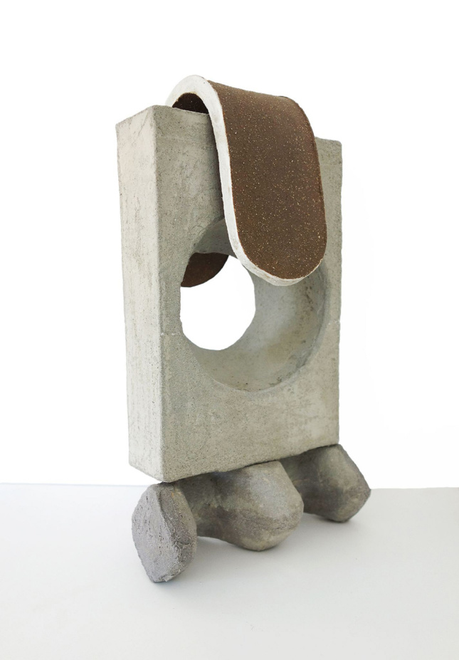 一个雕塑的近距离照片——一块长方形的混凝土，上面有一个圆形的洞，上面有一个厚厚的棕色釉面陶瓷舌头状的卵形。