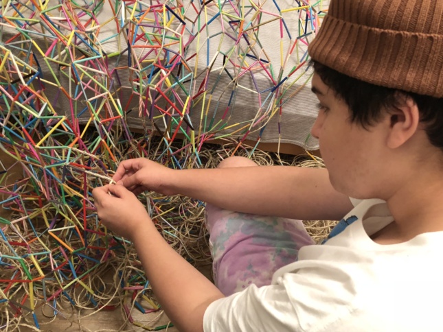 一个少年正在用彩色塑料吸管编织一张网