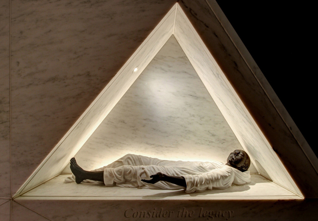 一个黑人斜倚在三角形切割结构中的雕塑照片。