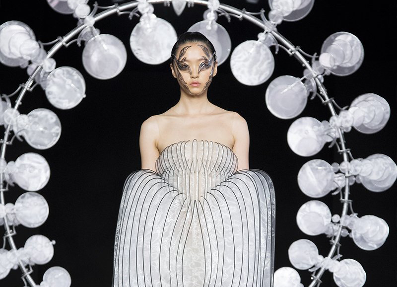 一名模特穿着有结构的宽缝连衣裙，穿过由艾丽斯·范·赫彭设计的旋转丝叶环