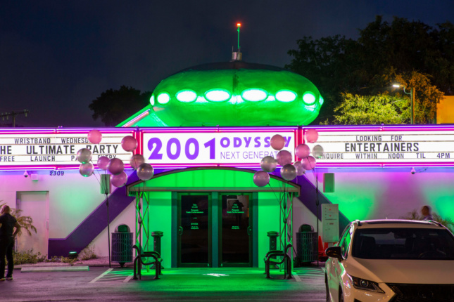 一个由绿色霓虹灯照明的脱衣舞俱乐部，顶部有一个类似ufo的未来屋