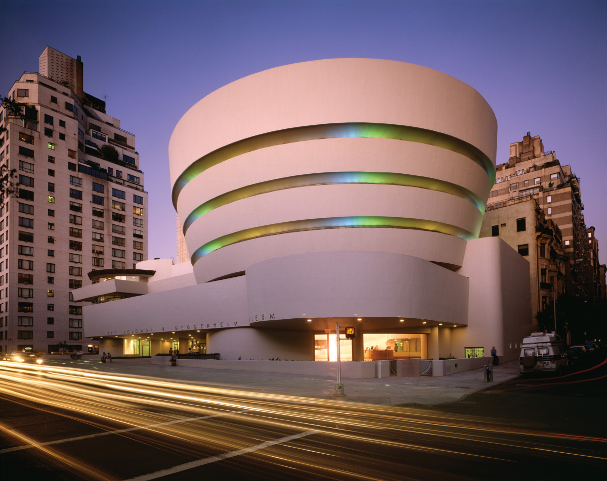 A large white, round building on a busy street corner, designed by Frank Lloyd Wright