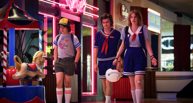 三位演员走在《怪奇物语》的片场，在霓虹灯闪烁的商场里