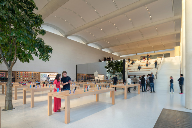 苹果商店的内部拍摄，有树，木制展示桌，台地座位