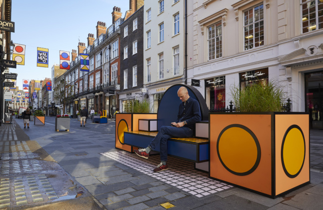 一个男人坐在伦敦设计节上的橙色长凳上的照片