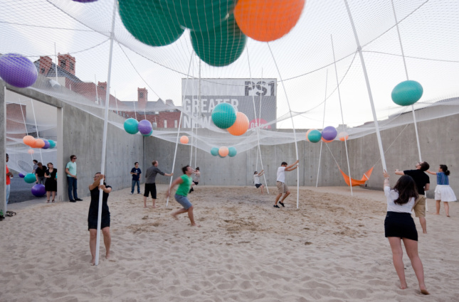 人们在装满沙滩球的网下玩沙子