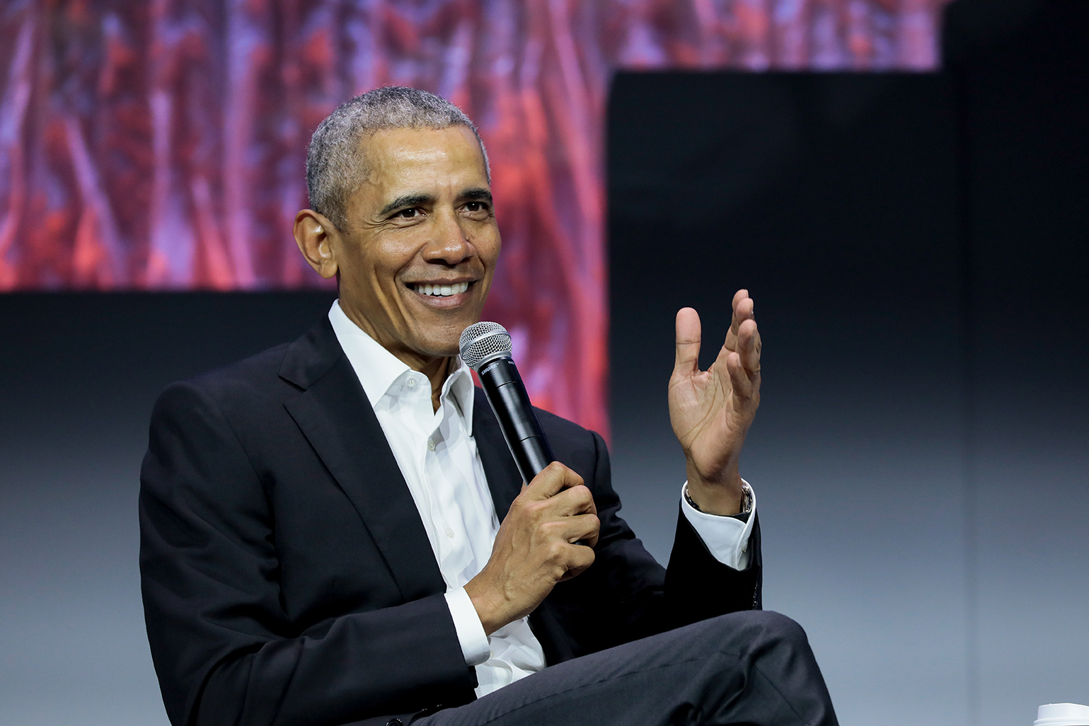 奥巴马总统坐在2019绿色建设大会上拿着麦克风做主题演讲