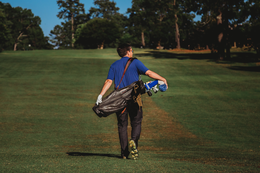 男子背着包走在高尔夫球场上的形象