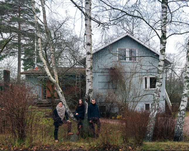 三位建筑策展人在树林里的木结构房屋前的图像