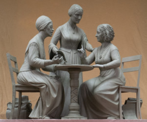 两个女人坐在一张桌子旁，第三个女人站在桌子后面