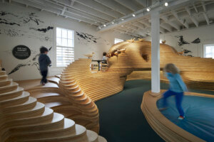 孩子们在新湾区发现博物馆空间内的木制游戏结构上嬉戏
