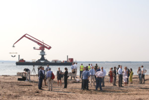 人们聚集在海滩上参加一个活动，背景是起重机