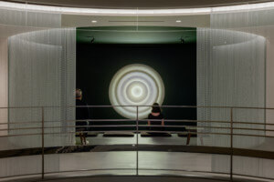 一个博物馆画廊的内部照片，在它的中心有一个明亮的光雕塑，在曼荼罗实验室的薄纱布窗帘的框架下