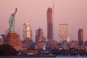 一座高大细长的摩天大楼，前景是自由女神像