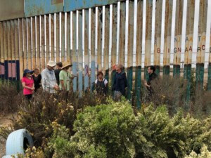 人们站在横跨美墨边境的栅栏旁