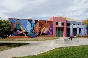 a skatepark with a large mural and colorful post-modernist building in the background