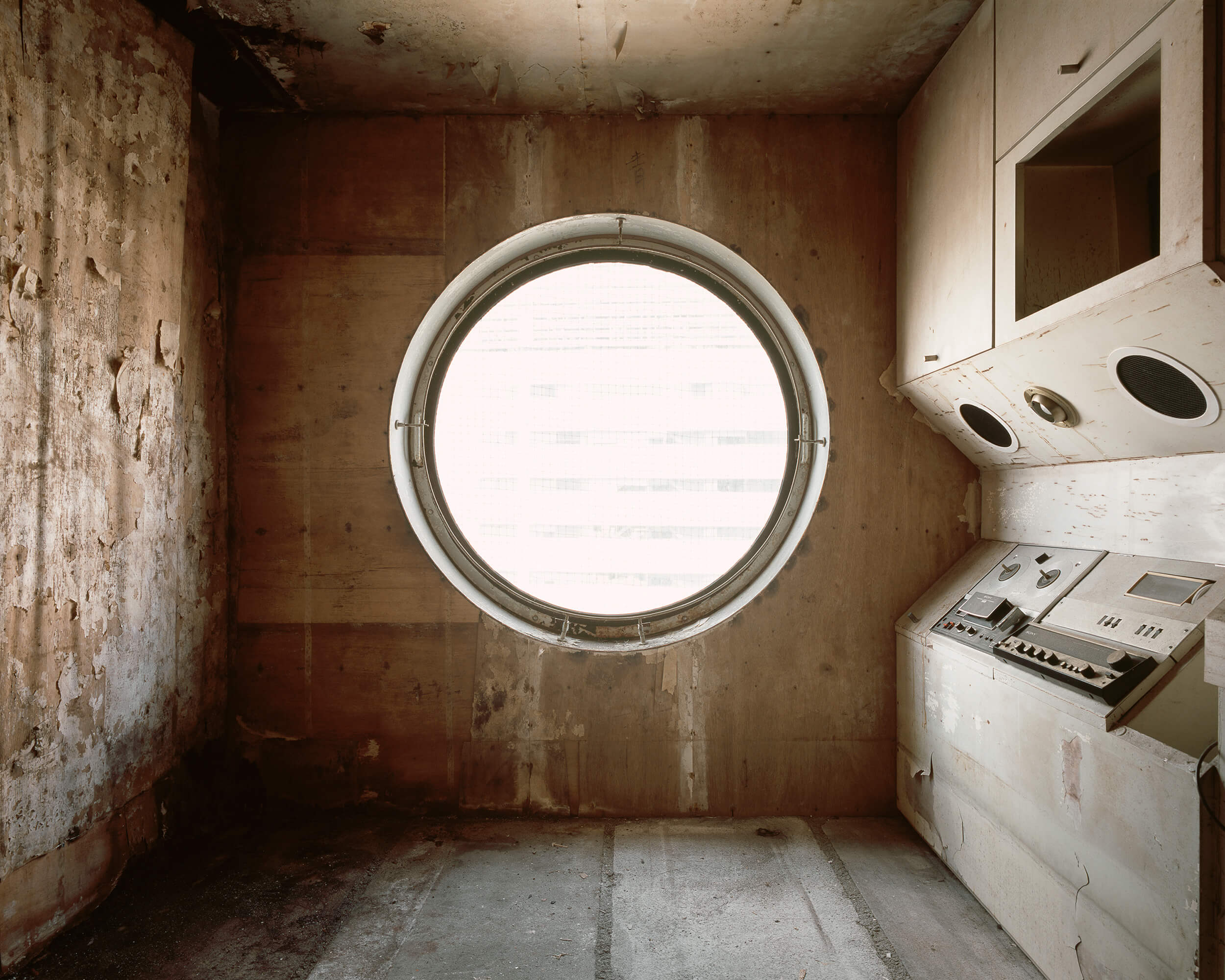 通过一个大的圆形窗户，可以看到一个废弃的、腐朽的生活空间