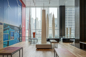 installation view of an exhibition on building energy with chicago skyscrapers seen through a window