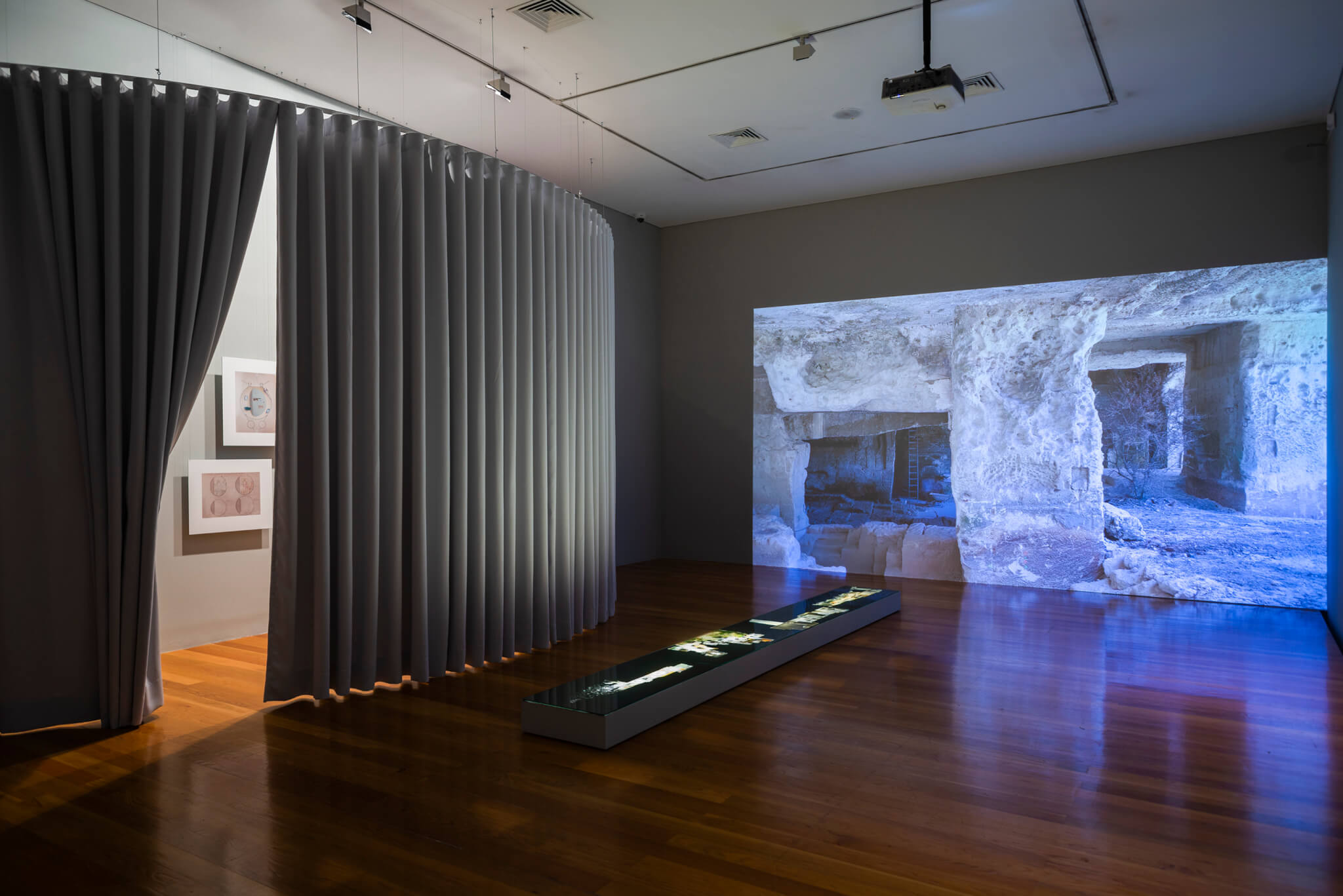 幕布分隔了黑暗的展览空间，远处的墙壁上有视频投影