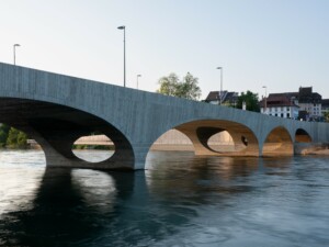 A concrete bridge gently arches over a river in Switzerland
