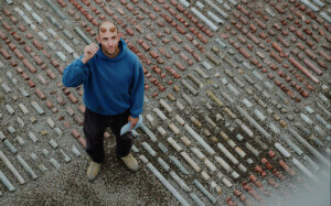 Man wearing a blue shirt looks above to the camera while standing on an installation of bedrock samples.